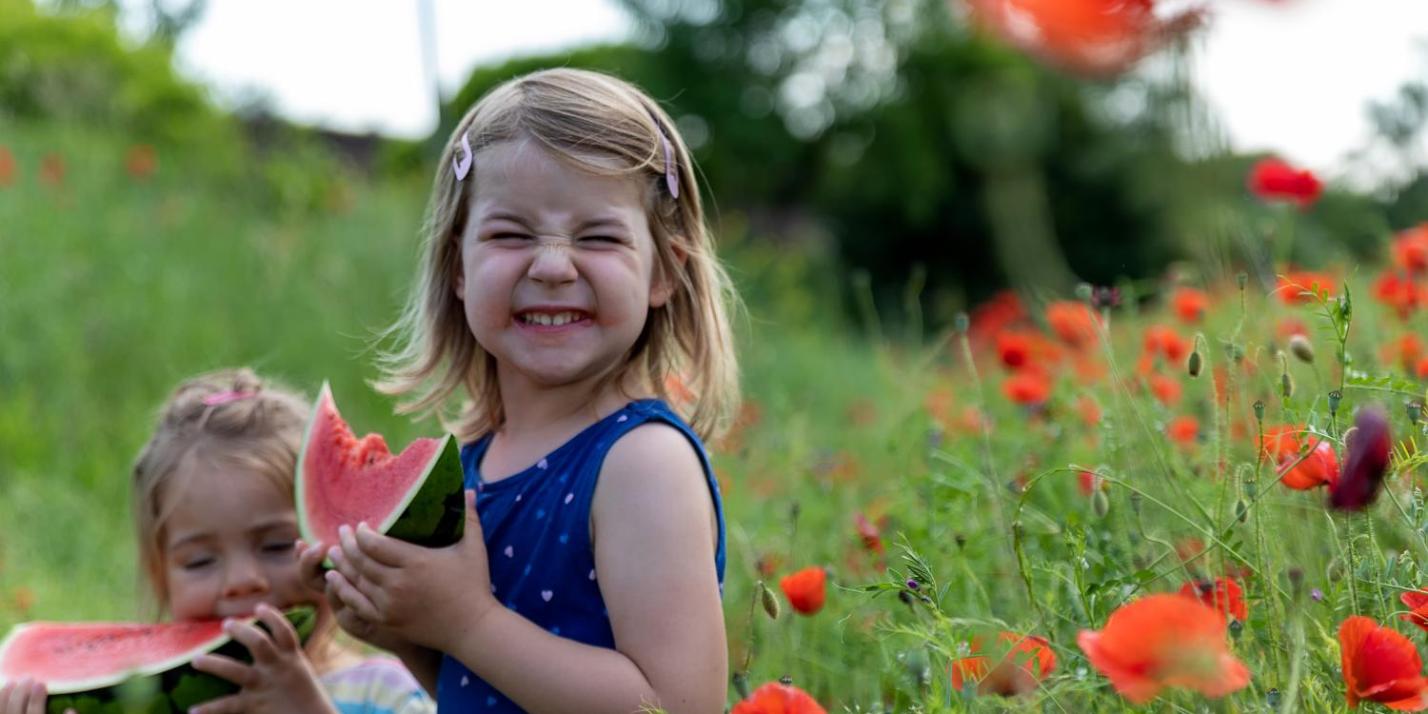 Ein kleines Mädchen freut sich über ein Stück Wassermelone in einem Mohnfeld