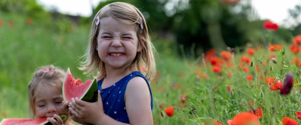 Ein kleines Mädchen freut sich über ein Stück Wassermelone in einem Mohnfeld