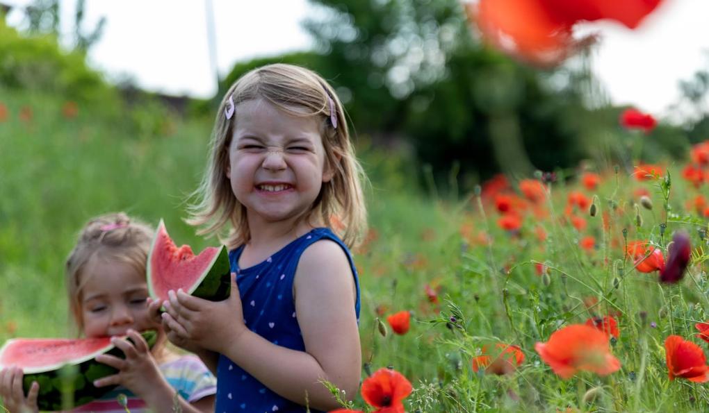 Ein kleines Mädchen freut sich über ein Stück Wassermelone in einem Mohnfeld