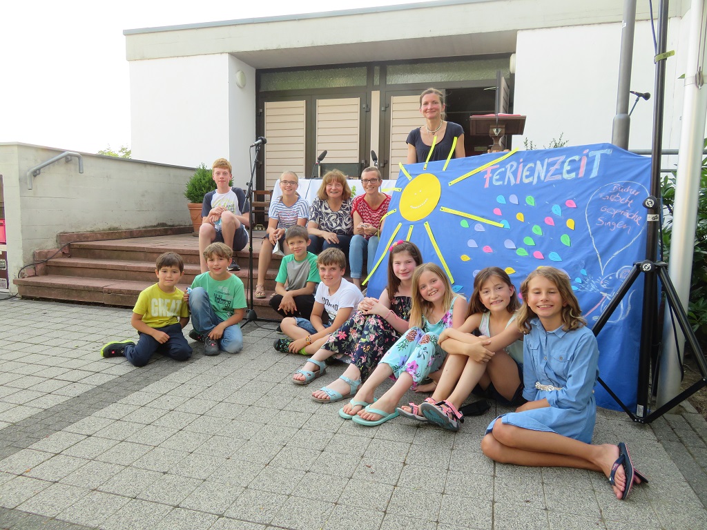 Mehrere Kinder sitzen vor einem blauen Tuch mit Sonne zum Thema Ferienzeit