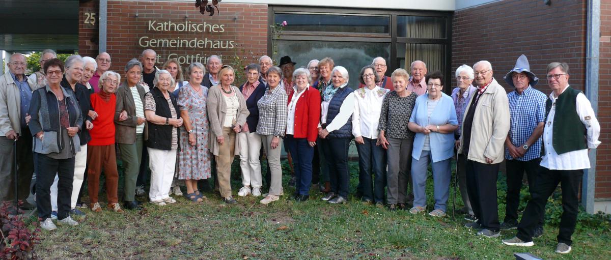 Rund 25 Mitglieder der Gruppe 50+ stehen im Halbkreis und lächeln in die Kamera.