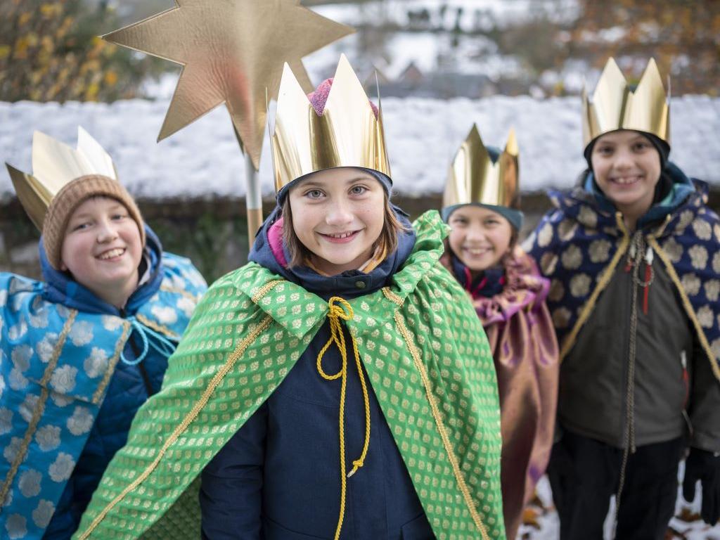 Vier Kinder, gekleidet als Sternsinger, laufen durch die Straße