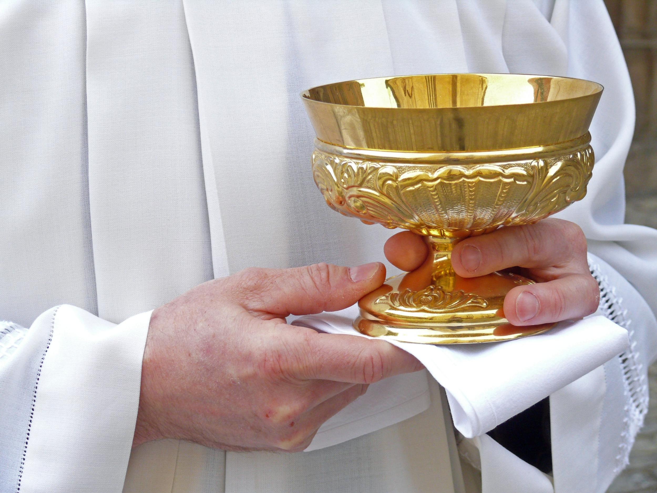 Person in weißem Messgewand trägt eine goldene Hostienschale.