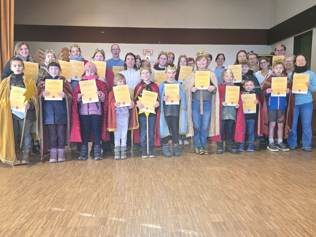 Eine Gruppe von Kindern, Jugendlichen und Erwachsenen, gekleidet als Sternsinger und mit Sternsinger-Urkunden