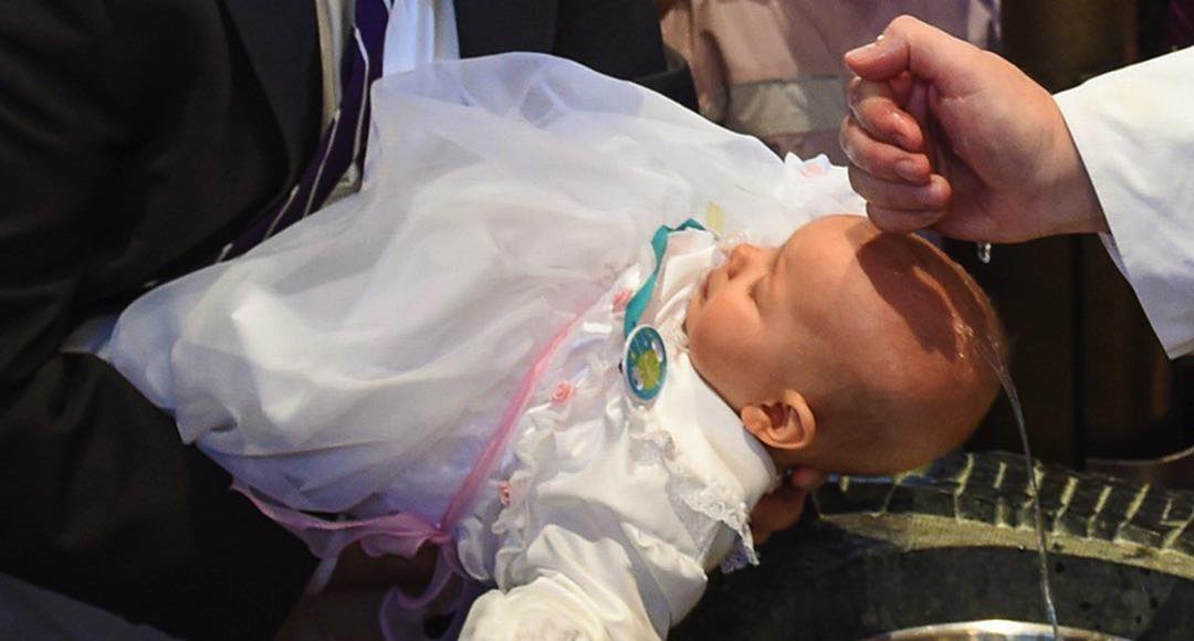 Pfarrer tauft Baby über Taufbecken.