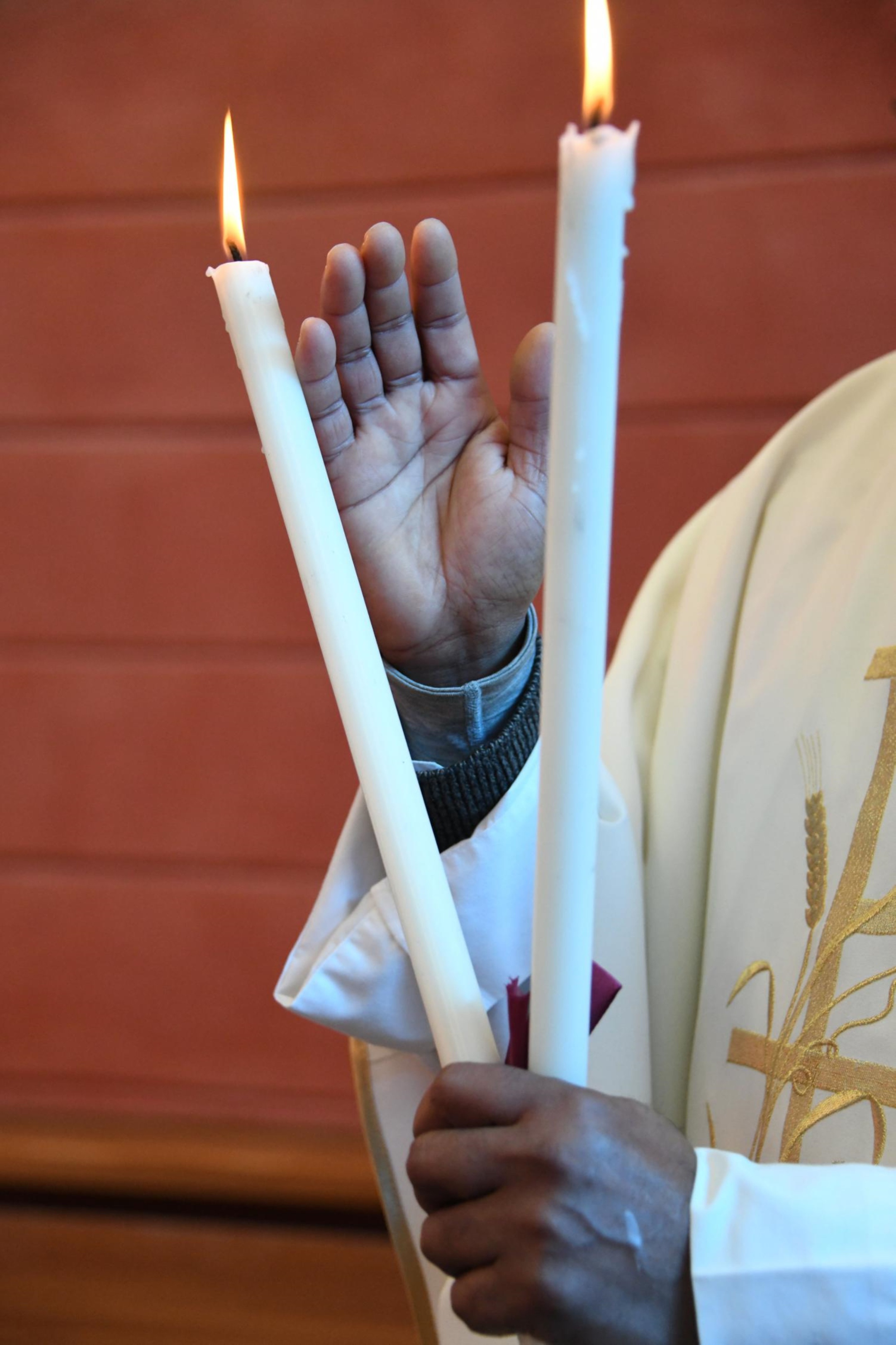 Ein Pfarrer hält zwei gekreuzte, brennende Kerzen in der Hand und erteilt den Blasiussegen.