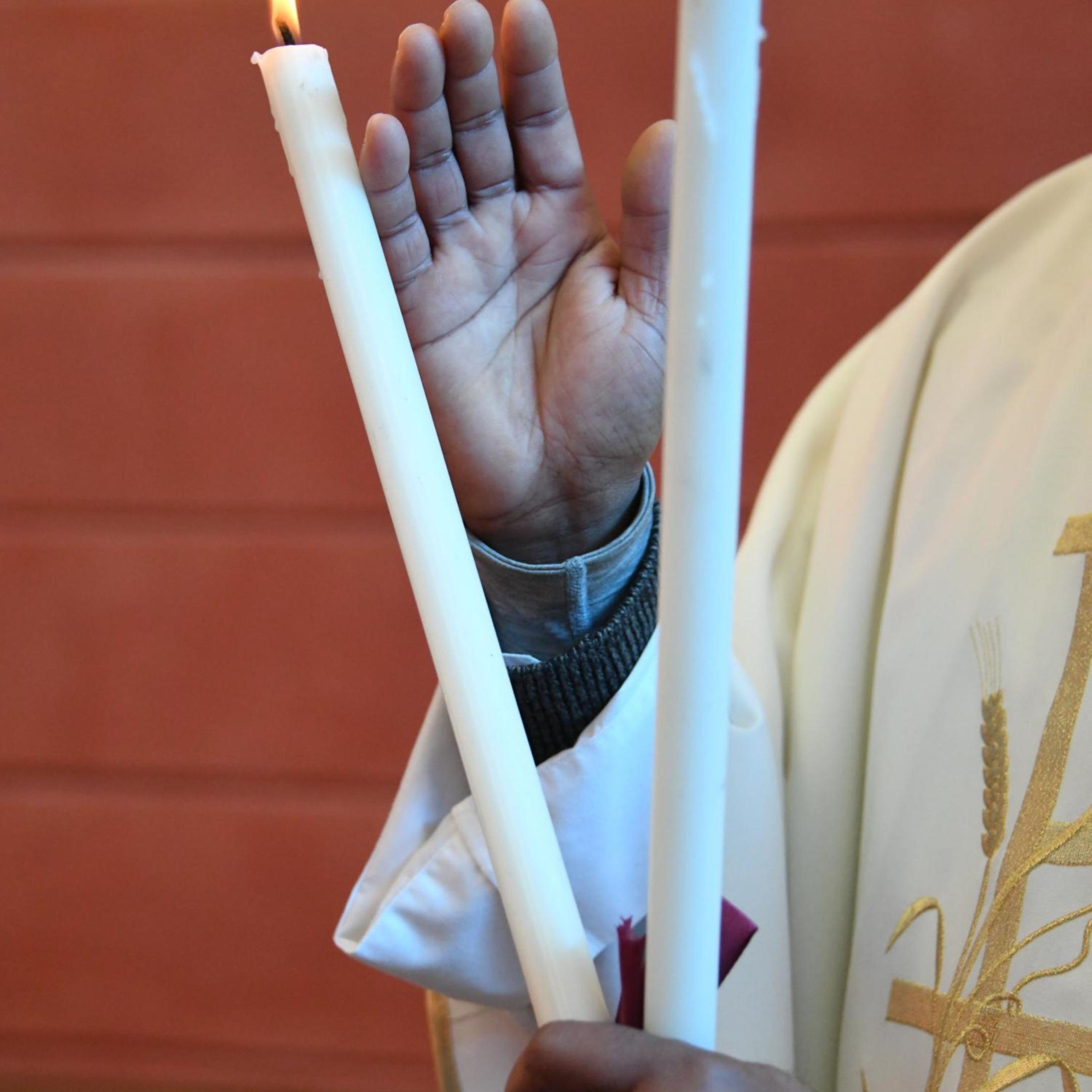 Ein Pfarrer hält zwei gekreuzte, brennende Kerzen in der Hand und erteilt den Blasiussegen.