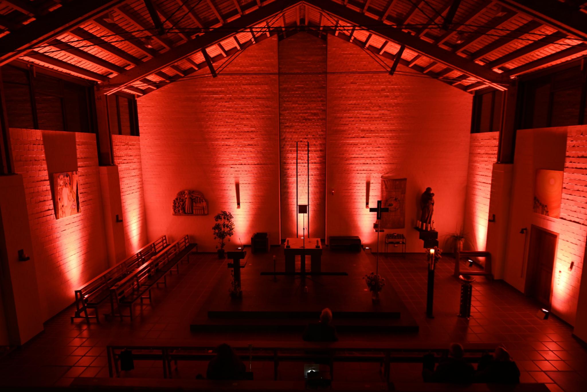 Blick von der Empor in den Altarraum, dieser ist mit roten Strahlern stimmungsvoll beleuchtet