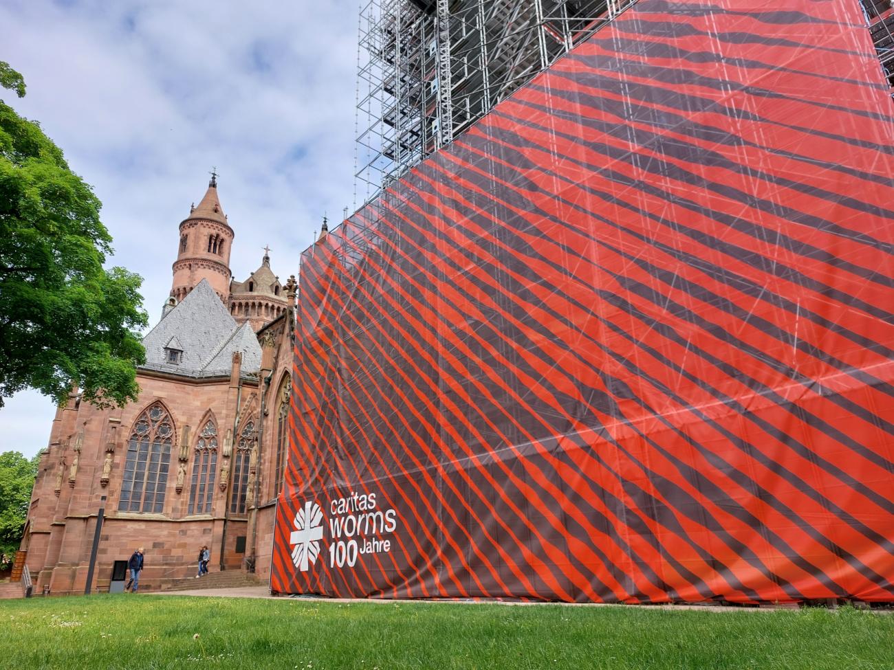 2025-05-19_pm_jubiläumswochenende_cv-worms_foto1 (c) Caritasverband Worms e.V. 100 Jahre Caritas in Worms – das feiert der Sozialverband mit einem großen Fest-wochenende am 23. und 24. Mai 2025 rund um den Dom. Dort weißt bereits seit einigen Wochen ein 300 Quadratmeter großes Caritas-Banner auf das besondere Jubiläum hin.