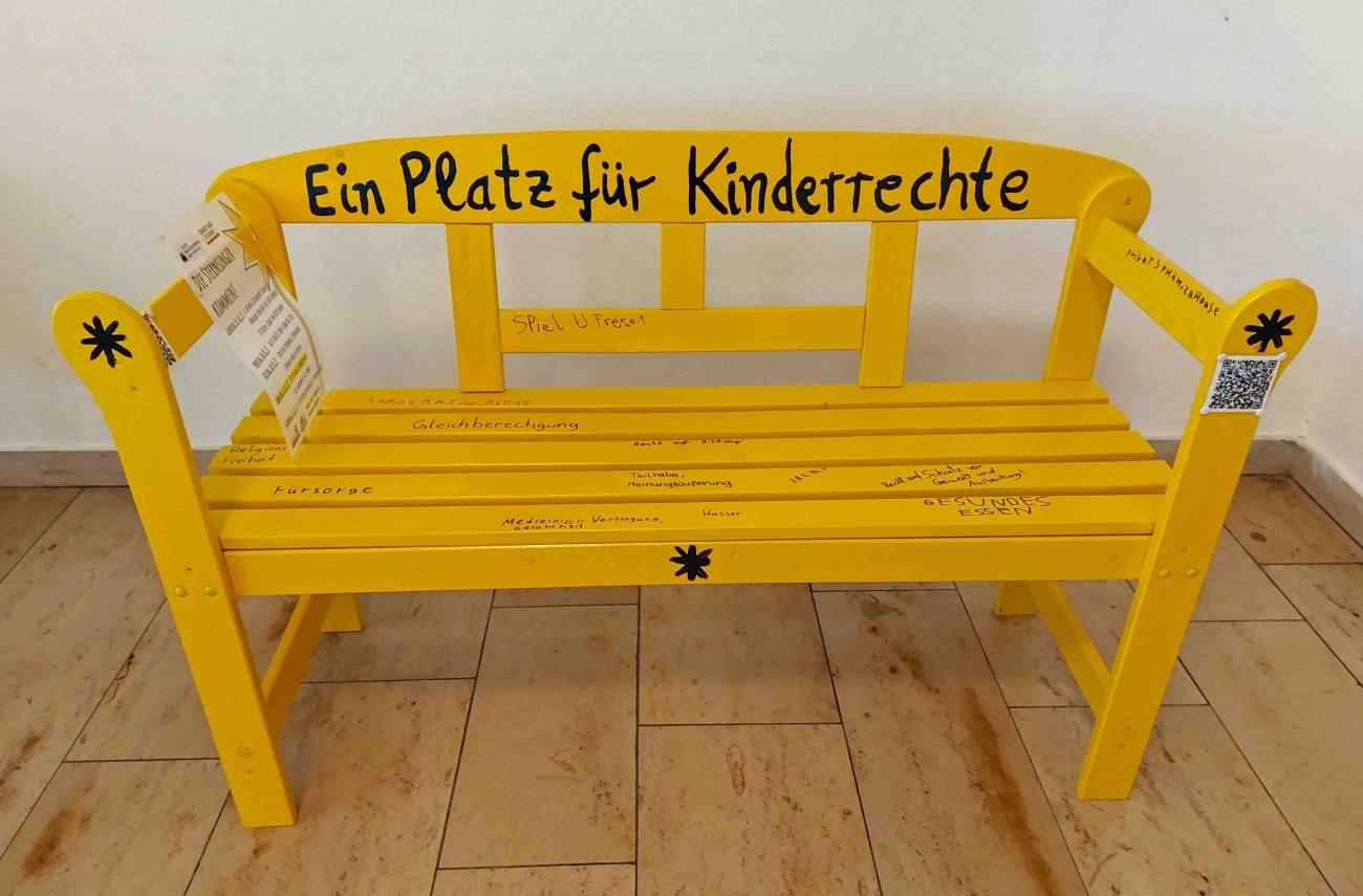 Ein symbolhafter 'Platz für Kinderrechte'. Die gelbe Bank wird bei der Aktion 2025 immer wieder sichtbar sein.