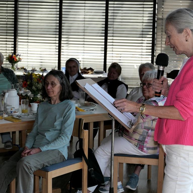 Eine Frau am Rednerpult spricht über ein Mikro zu Frauen, die an Tischen sitzen.