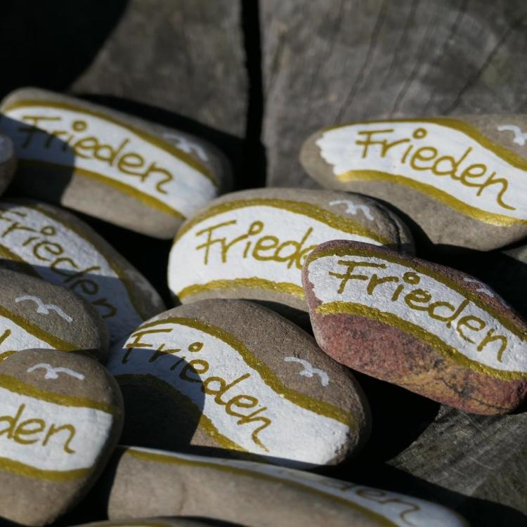 Große Kieselsteine, bemalt mit dem Wort Frieden in Gold und Weiß