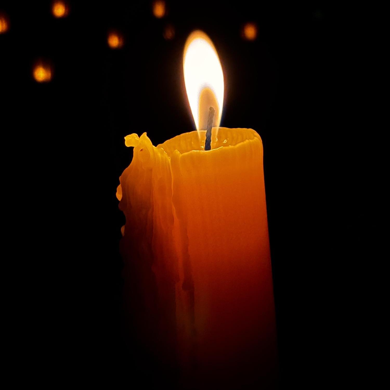 Eine Kerze leuchtet vor dunklem Hintergrund, in dem in der Ferne weitere Lichter zu erkennen sind