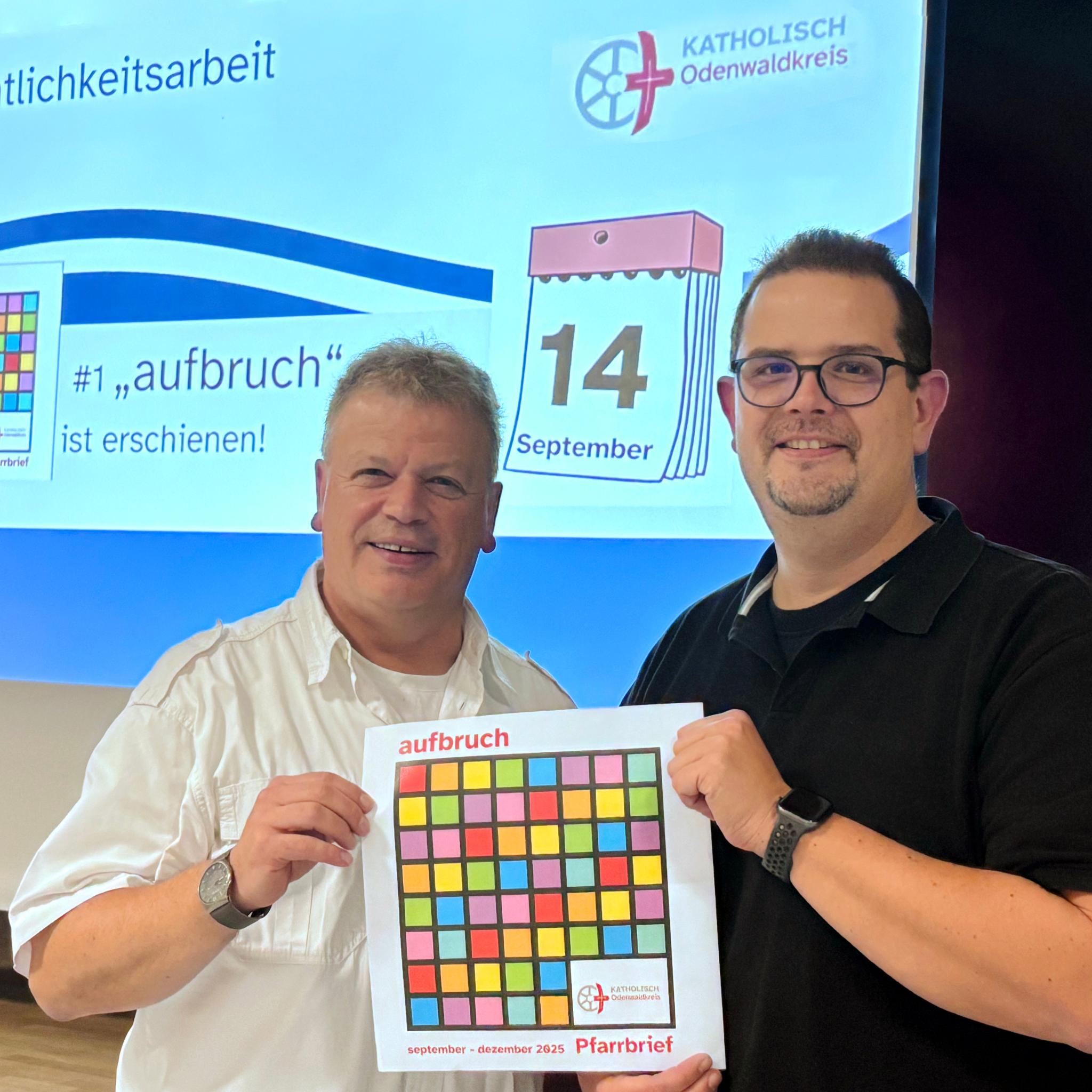 Leitender Pfarrer Harald Poggel und Verwaltungsleiter Matthias Kusch vor Projektionswand zeigen das Titelblatt des neuen Pfarrbriefs