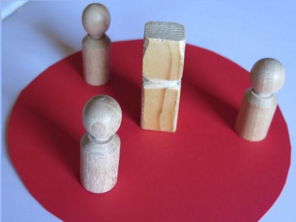 Drei Holzfiguren srehen um einen Holzklotz