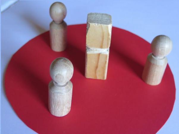 Drei Holzfiguren srehen um einen Holzklotz