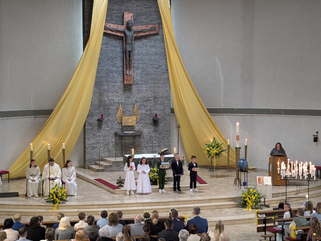 Kommunionkinder halten Kerze, kleine Flasche Weihwasser, Mauerstein, Mappe der Vorbereitungszeit (c) up