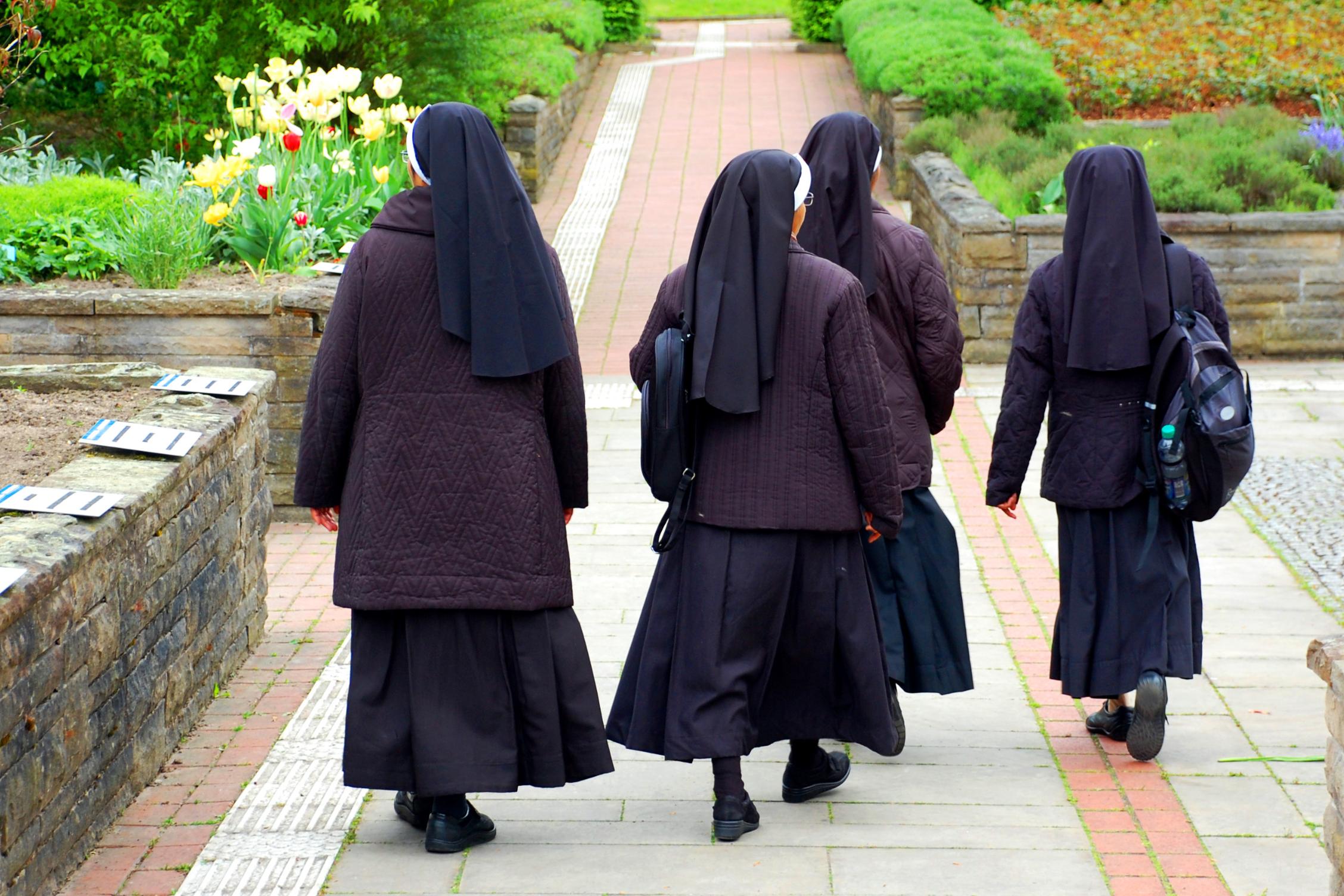 Nonnen in Ordenstracht laufen durch Kräutergarten