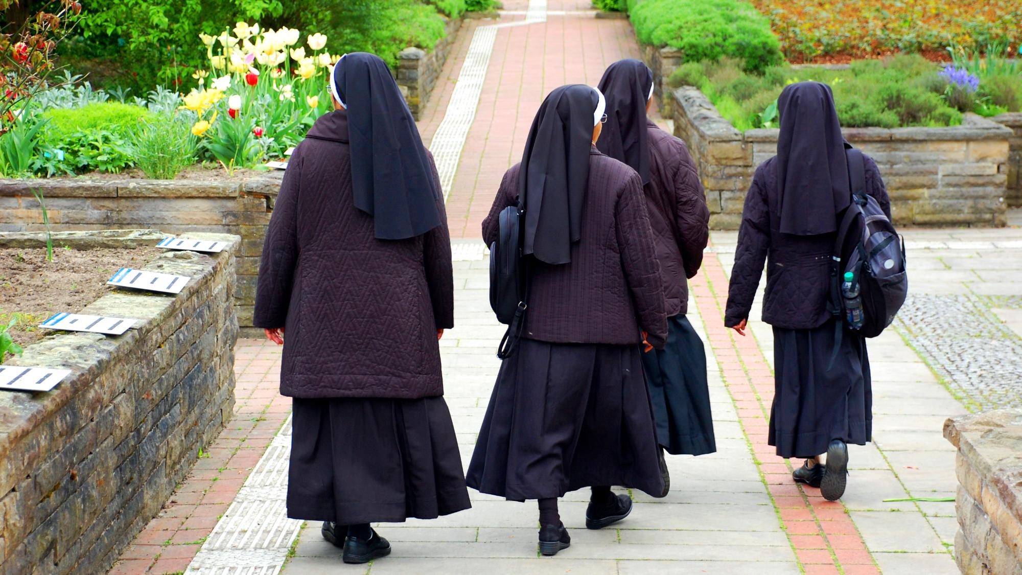 Nonnen in Ordenstracht laufen durch Kräutergarten