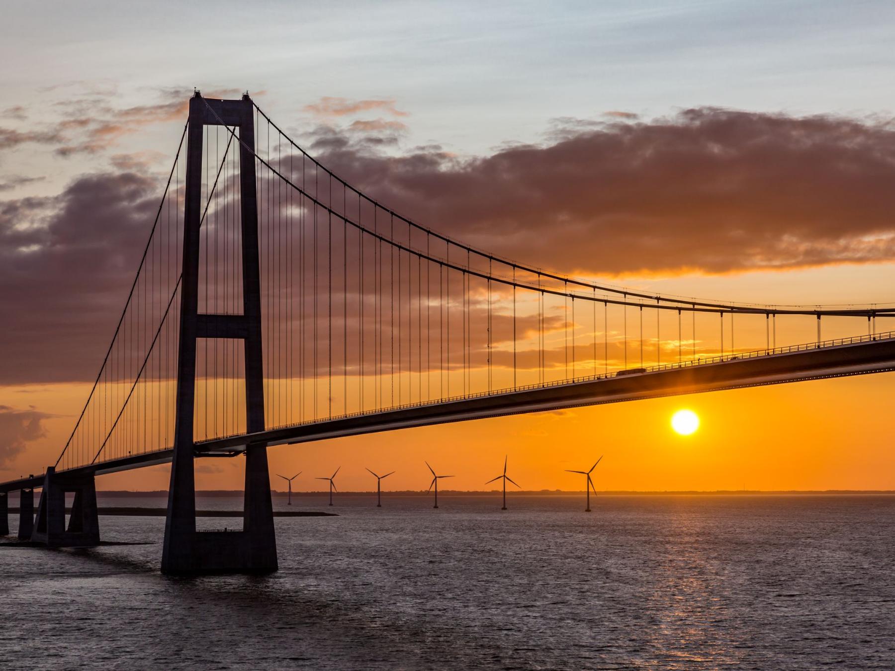 Brücke übers Meer im Sonnenuntergang, im Hintergrund Windräder
