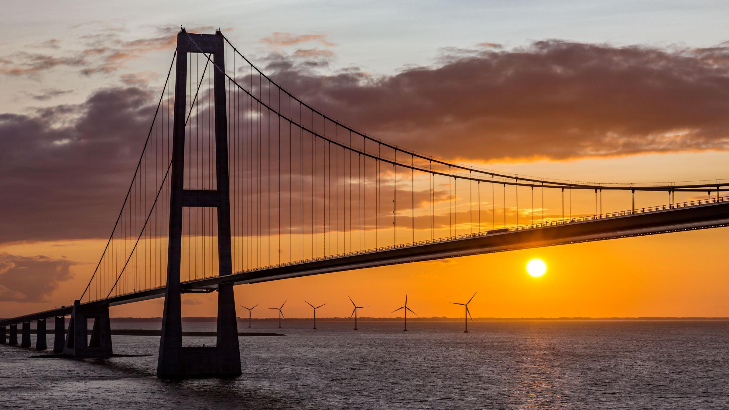Brücke übers Meer im Sonnenuntergang, im Hintergrund Windräder