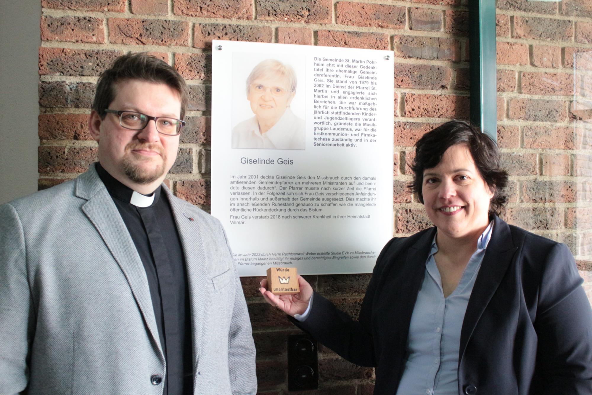 Pohlheim, 25. Februar 2024: Pfarrer Martin Sahm (links) und die Bevollmächtigte Stephanie Rieth vor der Gedenktafel für Giselinde Geis im Pfarrzentrum von St. Martin.