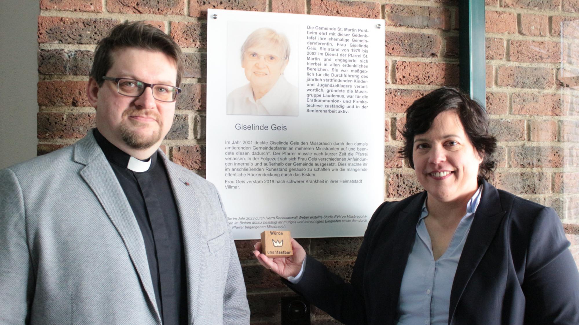 Pohlheim, 25. Februar 2024: Pfarrer Martin Sahm (links) und die Bevollmächtigte Stephanie Rieth vor der Gedenktafel für Giselinde Geis im Pfarrzentrum von St. Martin.