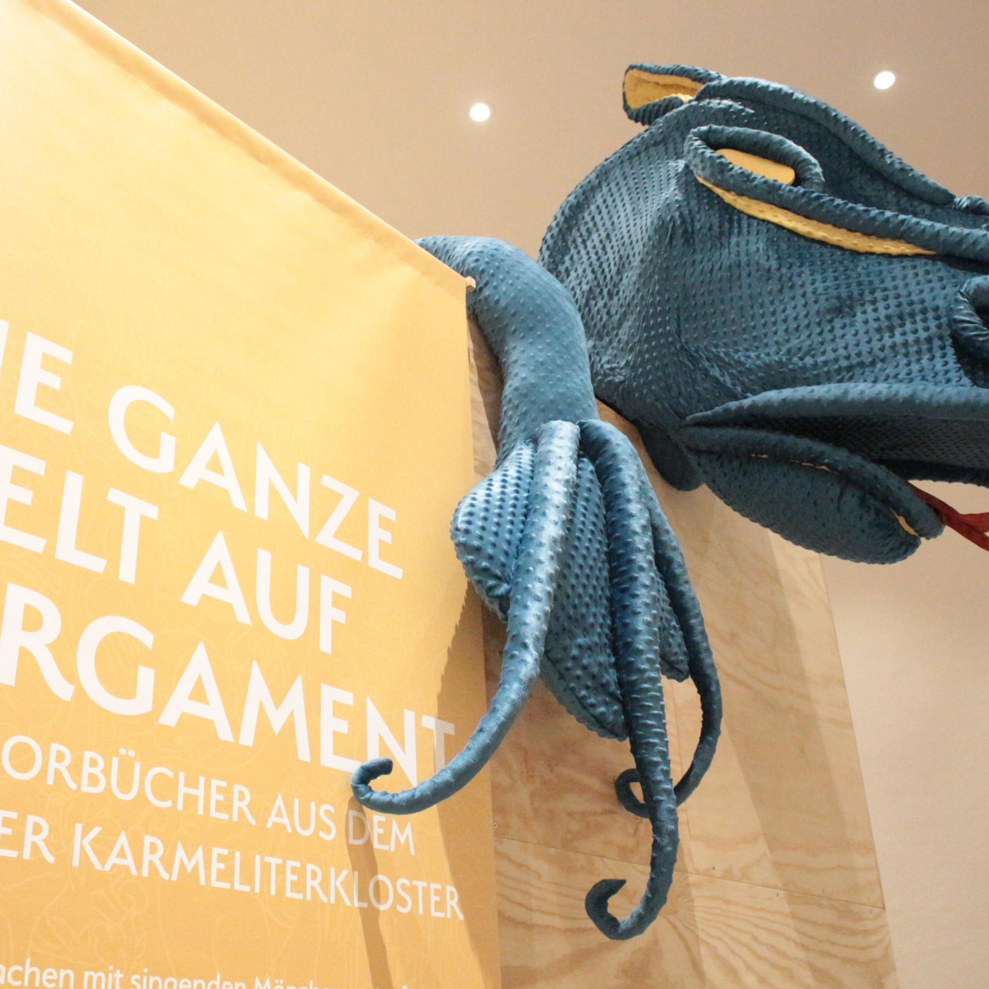 Mainz, 6. November 2024: Die Ausstellungsbesucher werden im Mainzer Dom- und Diözesanmuseum von einem großen blauen Drachen beim Rundgang zu den Karmeliter Chorbüchern begrüßt.