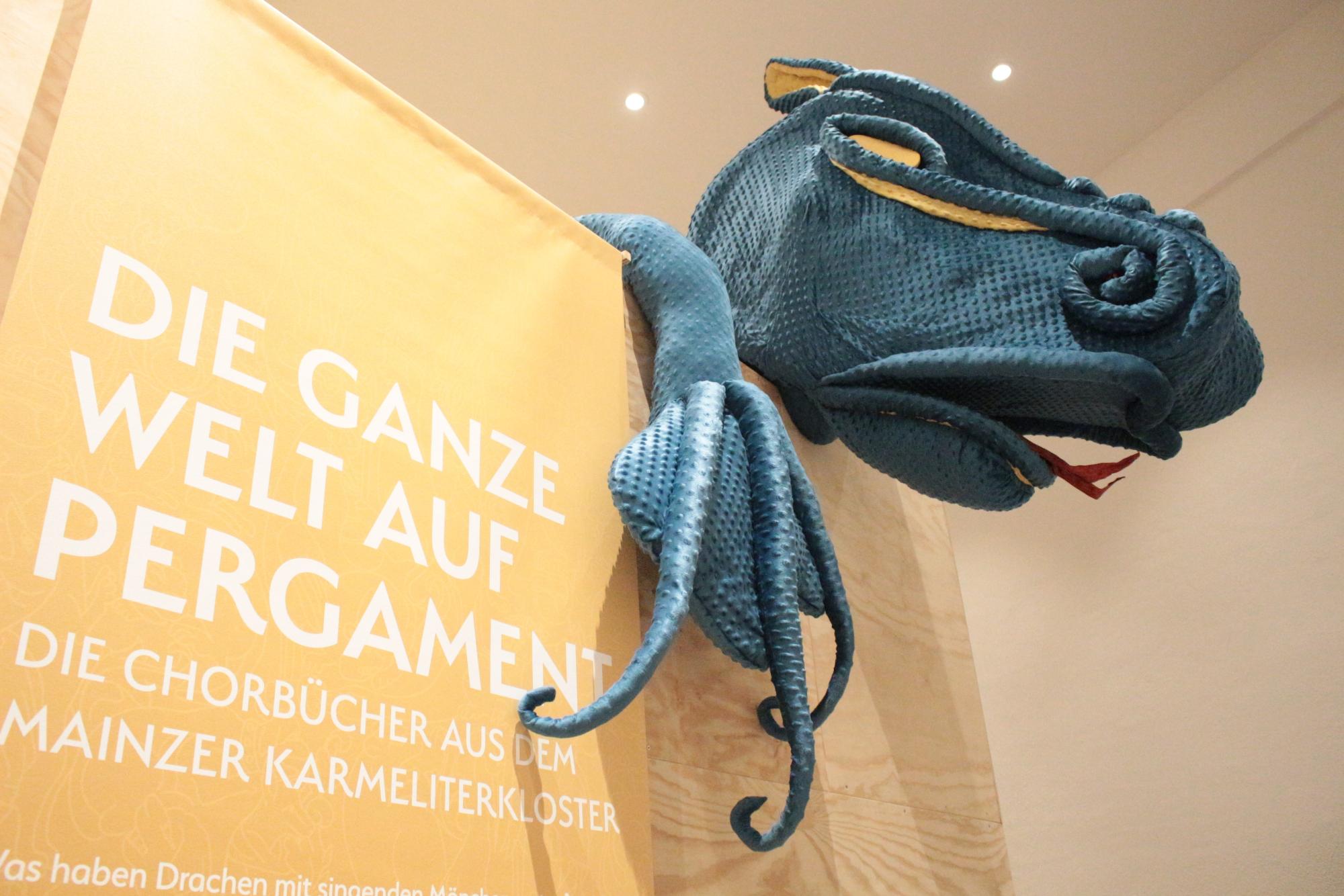 Mainz, 6. November 2024: Die Ausstellungsbesucher werden im Mainzer Dom- und Diözesanmuseum von einem großen blauen Drachen beim Rundgang zu den Karmeliter Chorbüchern begrüßt. (c) Bistum Mainz / Blum