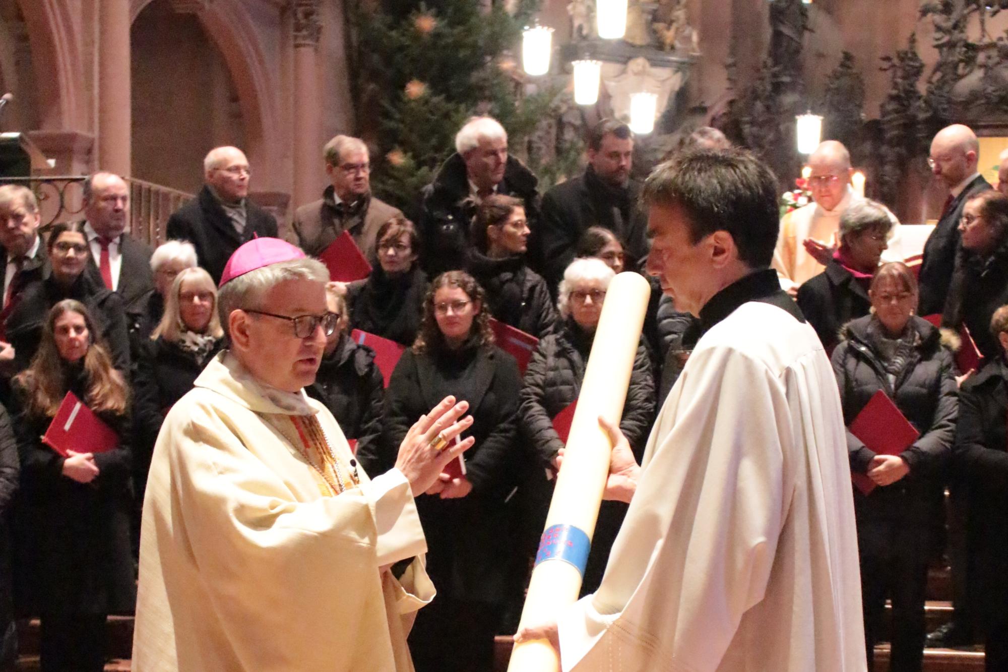 Mainz, 29. Dezember 2024: Bischof Peter Kohlgraf segnete zu Beginn des Gottesdienstes die Heilig Jahr-Kerze, die vom Bischöflichen Zeremoniar, Pastoralreferent Johannes Brantzen, gehalten wird.