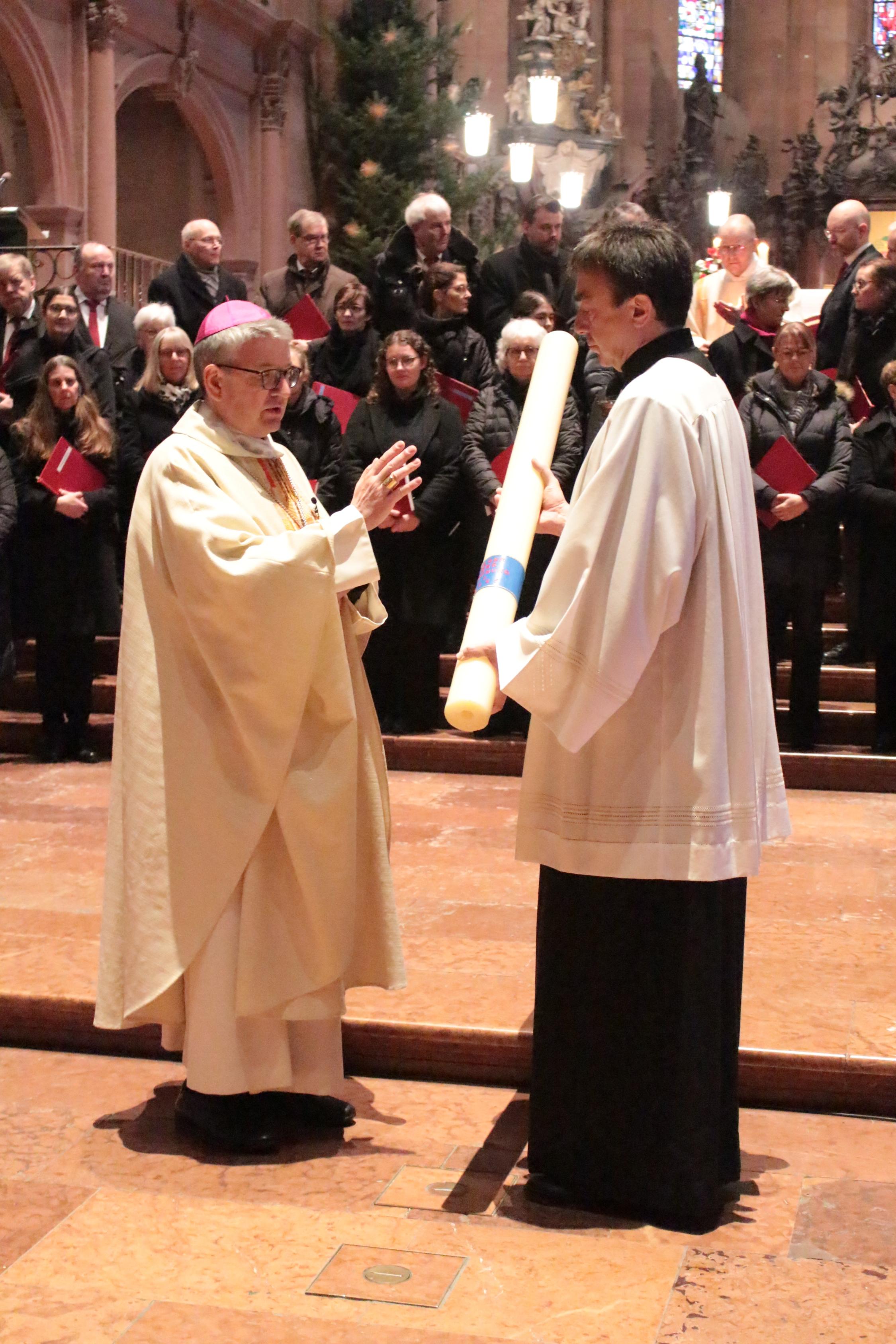 Mainz, 29. Dezember 2024: Bischof Peter Kohlgraf segnete zu Beginn des Gottesdienstes die Heilig Jahr-Kerze, die vom Bischöflichen Zeremoniar, Pastoralreferent Johannes Brantzen, gehalten wird.