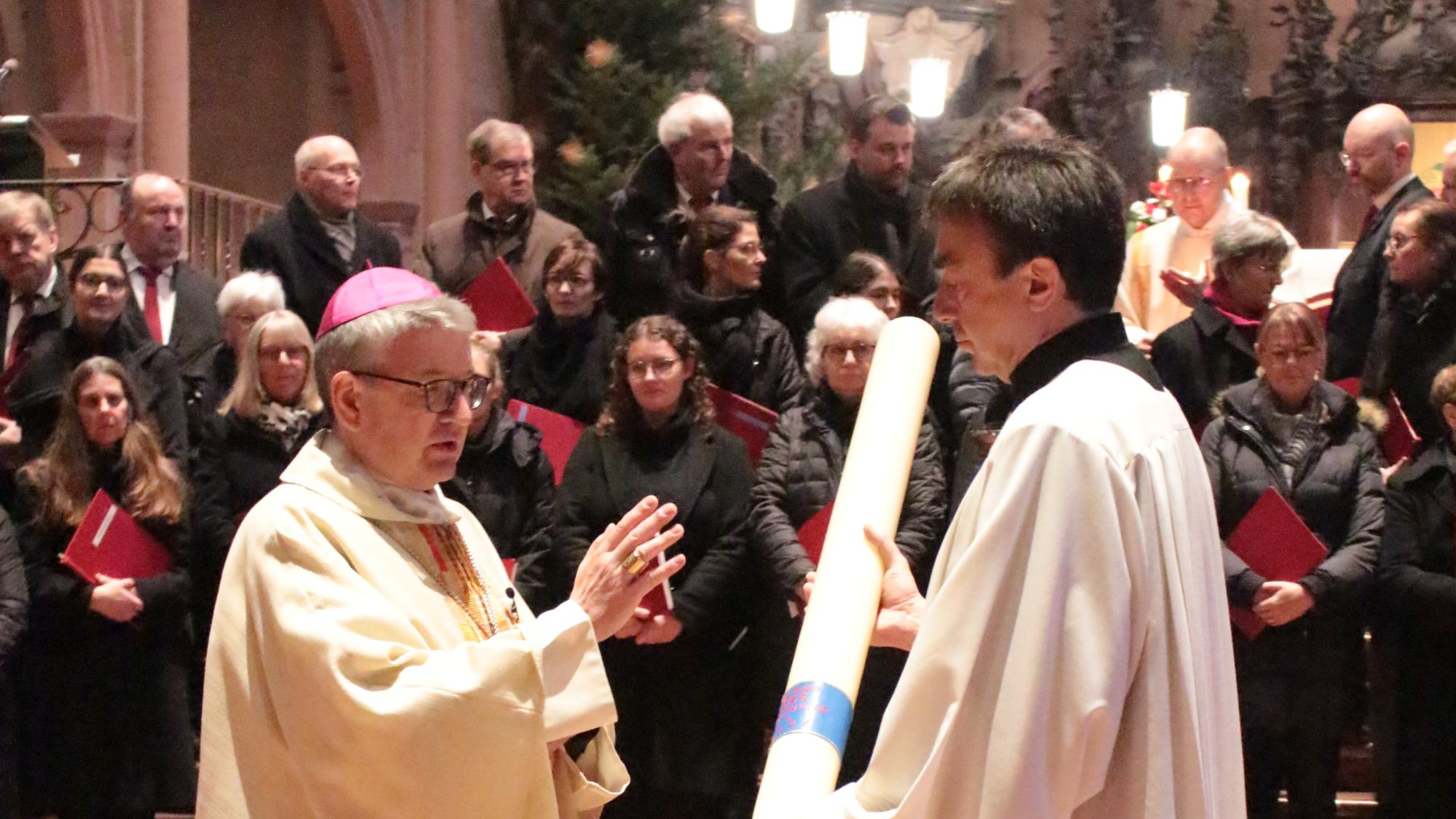 Mainz, 29. Dezember 2024: Bischof Peter Kohlgraf segnete zu Beginn des Gottesdienstes die Heilig Jahr-Kerze, die vom Bischöflichen Zeremoniar, Pastoralreferent Johannes Brantzen, gehalten wird.