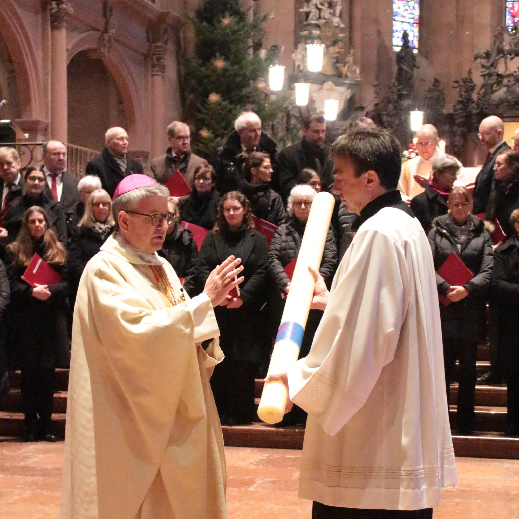 Mainz, 29. Dezember 2024: Bischof Peter Kohlgraf segnete zu Beginn des Gottesdienstes die Heilig Jahr-Kerze, die vom Bischöflichen Zeremoniar, Pastoralreferent Johannes Brantzen, gehalten wird.