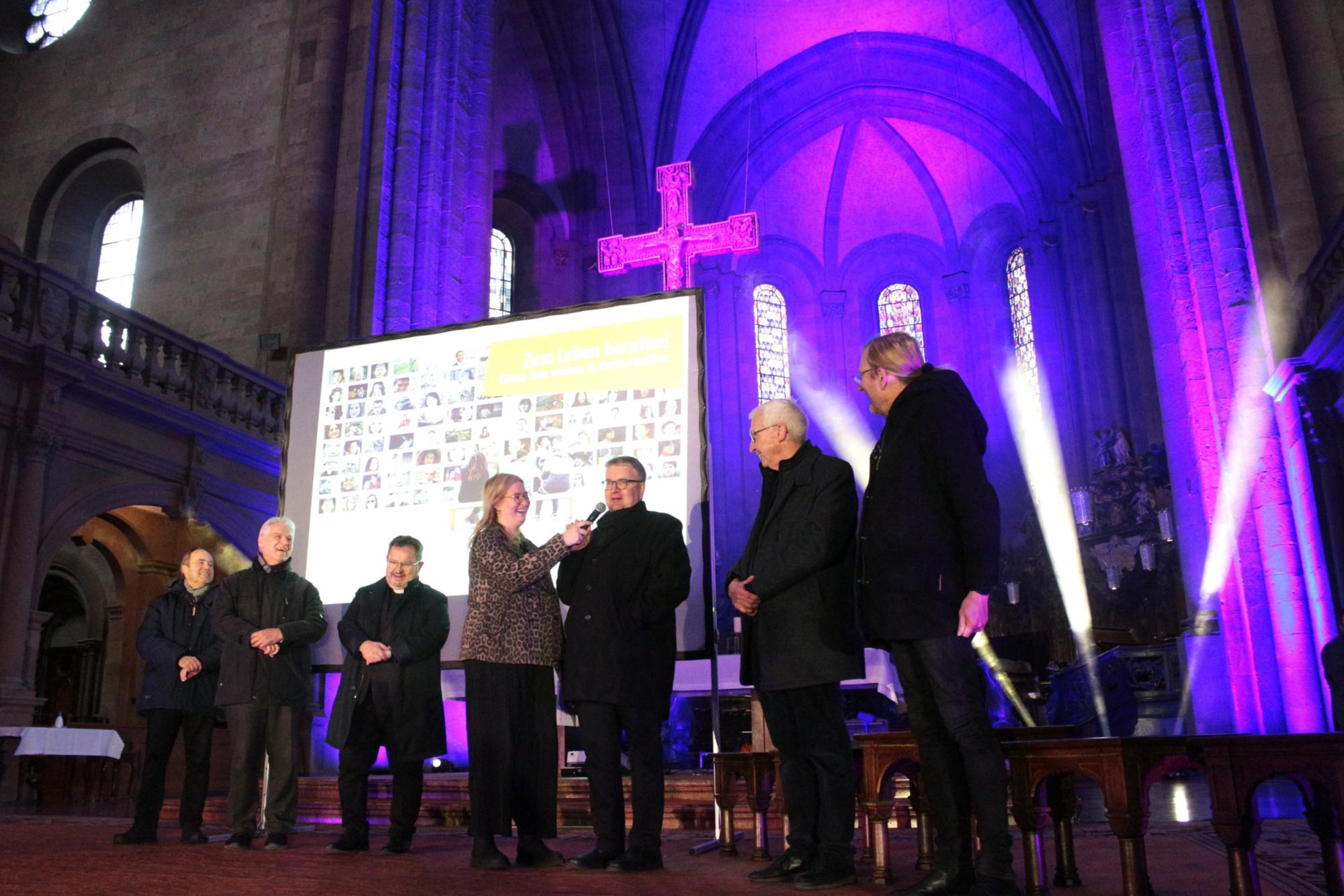 Mainz, 28. März 2026: Die Firmspender beim Auftakt des Firmbewerbertages im Mainzer Dom (v.l.n.r.): Klaus Forster, Michael Ritzert, Henning Priesel, Moderatorin Finja Fiedler, Bischof Peter Kohlgraf, Franz-Rudolf Weinert und Olaf Lindenberg. (c) Bistum Mainz / Blum
