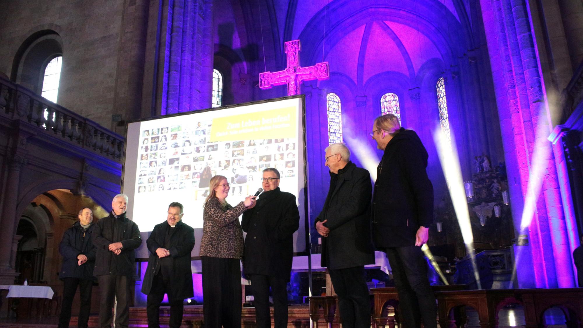 Mainz, 28. März 2026: Die Firmspender beim Auftakt des Firmbewerbertages im Mainzer Dom (v.l.n.r.): Klaus Forster, Michael Ritzert, Henning Priesel, Moderatorin Finja Fiedler, Bischof Peter Kohlgraf, Franz-Rudolf Weinert und Olaf Lindenberg.