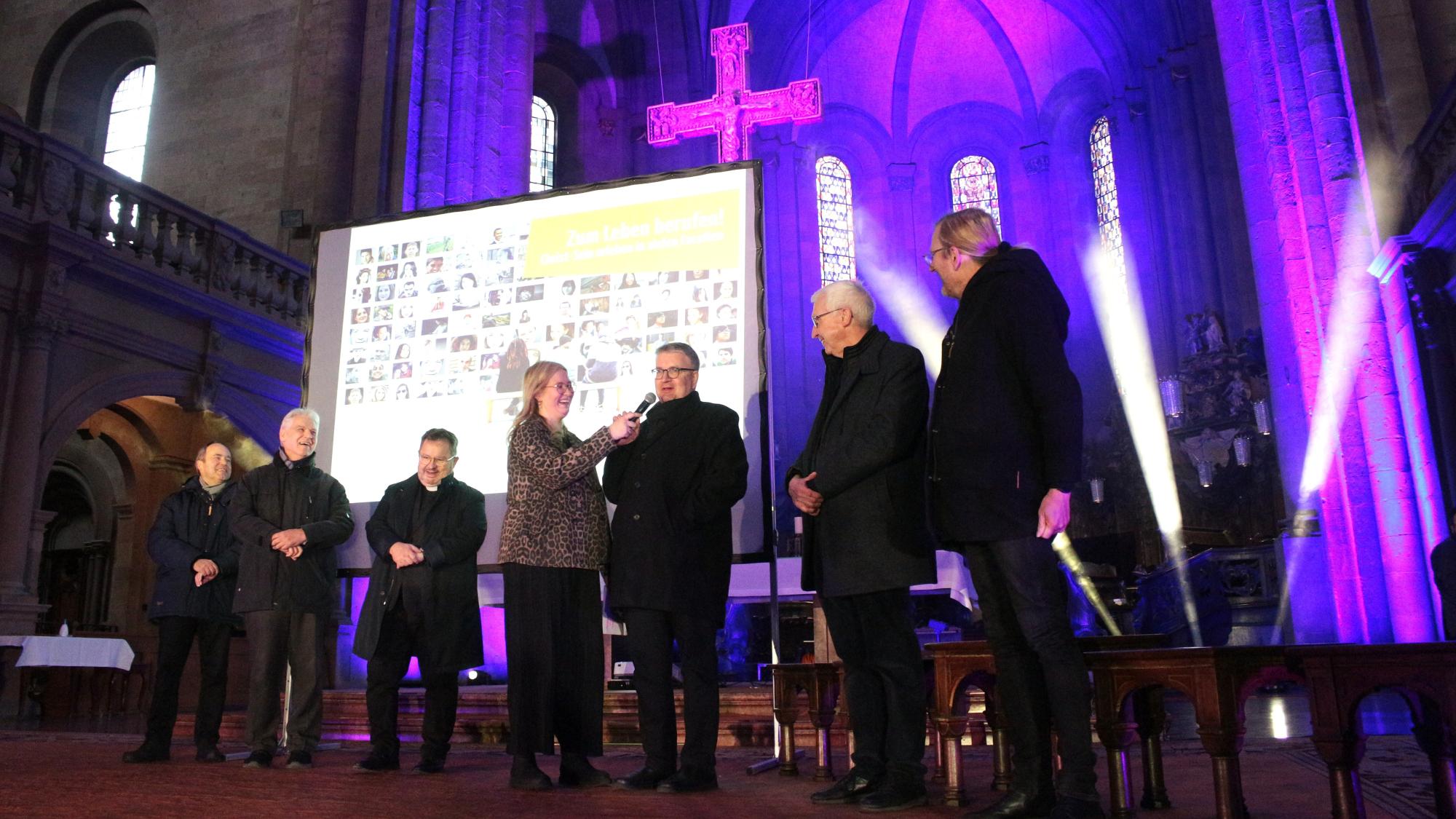 Mainz, 28. März 2026: Die Firmspender beim Auftakt des Firmbewerbertages im Mainzer Dom (v.l.n.r.): Klaus Forster, Michael Ritzert, Henning Priesel, Moderatorin Finja Fiedler, Bischof Peter Kohlgraf, Franz-Rudolf Weinert und Olaf Lindenberg.