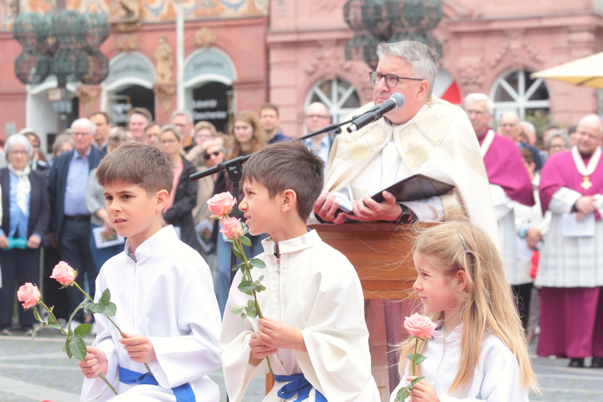 Mainz, 4. Juni 2026: Kinder aus den Gemeinden anderer Muttersprache brachten bei den Fürbitten auf dem Marktplatz Blumen zum Altar, dahinter Bischof Peter Kohlgraf. (c) Bistum Mainz / Blum
