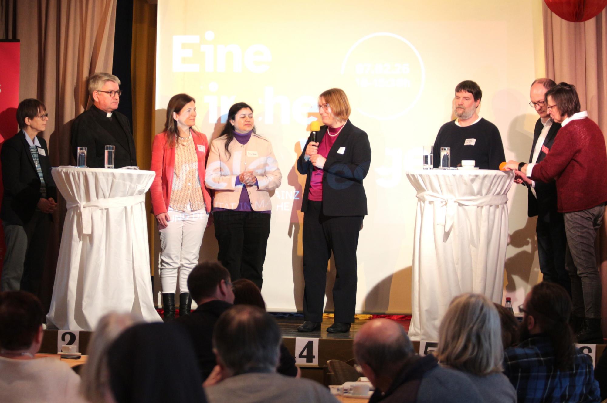 Mainz, 7. Februar 2026: Auf der Bühne des Kolpinghauses (v.l.n.r.): Schwester Birgit Weiler, Bischof Peter Kohlgraf, Meike Jolie Sana Iqbal, Regina Heyder Stephan Weidner, Andreas Linsenmann und Renate Flath. (c) Bistum Mainz / Blum