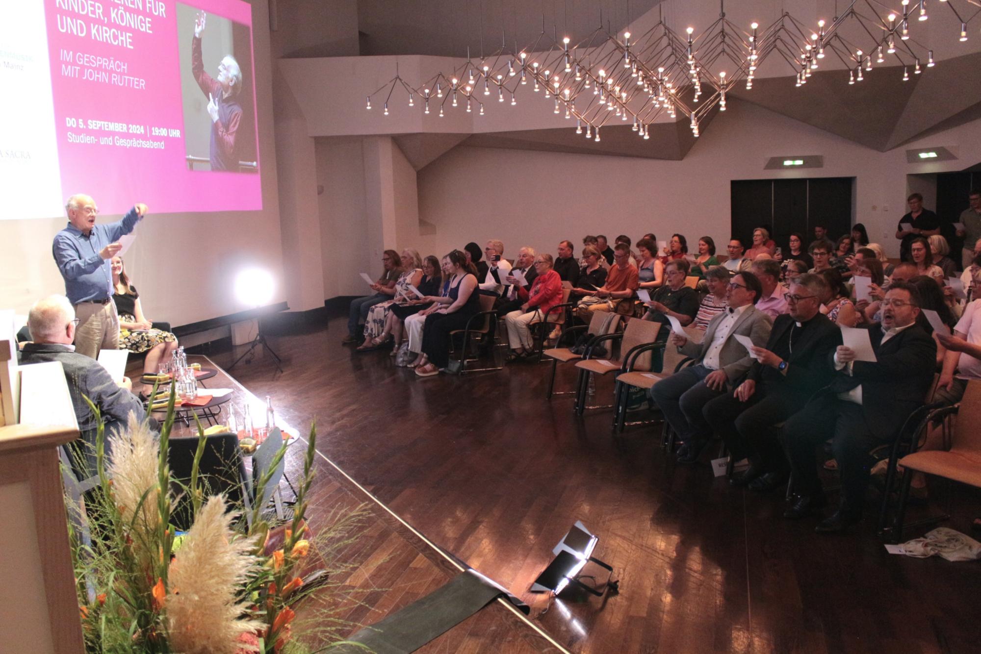 Mainz, 5. September 2024: Zum Abschluss wurde dann noch das Auditorium zum Chor, als Rutter den Saal zum Lied „Bleib bei uns, Herr“ dirigierte, begleitet von Walter Hirt am Flügel. (c) Bistum Mainz / Blum