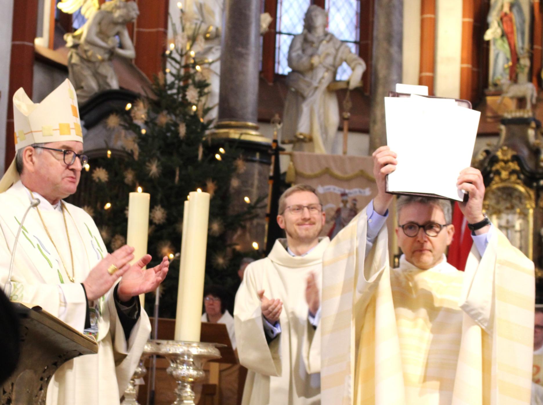 Bingen, 19. Januar 2025: Pfarrer Markus Lerchl hält die Gründungsurkunde der neuen Pfarrei Hl. Hildegard von Bingen, Rhein und Nahe in die Höhe, unter dem Beifall von Bischof Peter Kohlgraf (links) und Koordinator David Haub. (c) Bistum Mainz / Blum