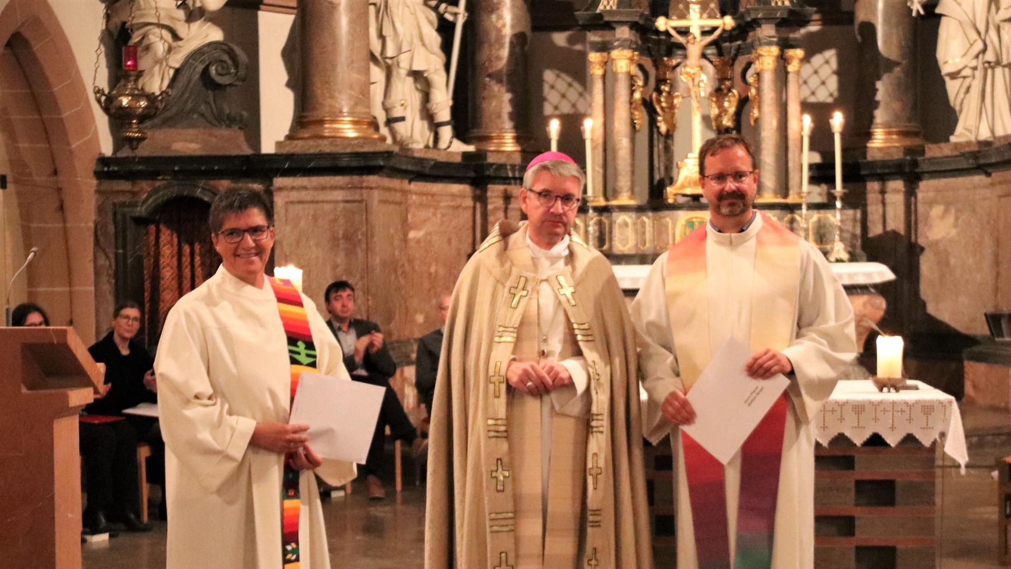 Bischof Peter Kohlgraf überreichte die Dekrete ihrer offiziellen Ernennung zu Beauftragten der queersensiblen Pastoral an Christine Schardt und Mathias Berger