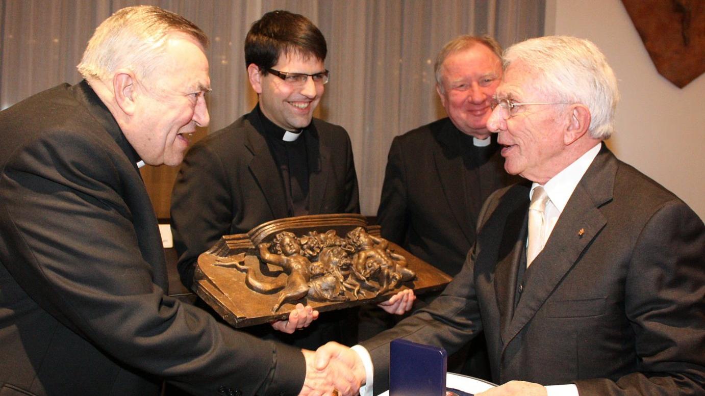 Mainz, 20. Januar 2013: Kardinal Karl Lehmann (links) würdigte das ehrenamtliche Engagement von Wolfgang Strutz (rechts) für die Mainzer Domstiftung; Bischofskaplan Johannes Zepezauer hält den Abguss der Misericordie des mittleren Sitzes aus dem Brendelschen Chorgestühl, den das Bistum Strutz geschenkt hat, daneben Generalvikar Dietmar Giebelmann.