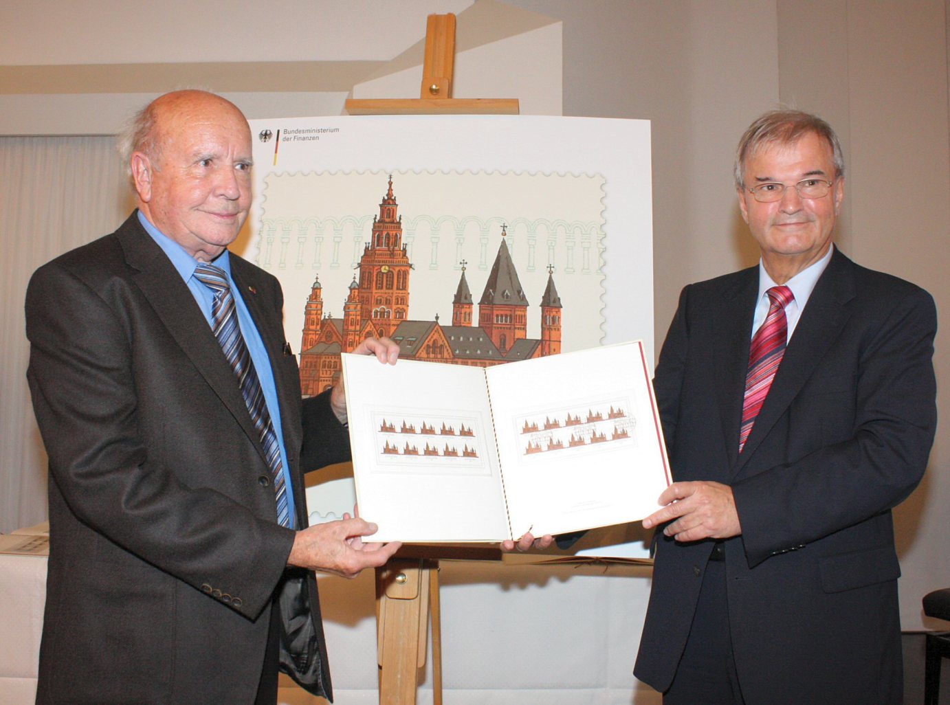 Mainz, 14. August 2009: Staatssektretär karl Diller (rechts) überreicht ein Album mit Erstdrucken an Professor Ernst Kößlinger, der die Mainzer Dom-Briefmarke gestaltet hat. (c) Bistum Mainz / Blum