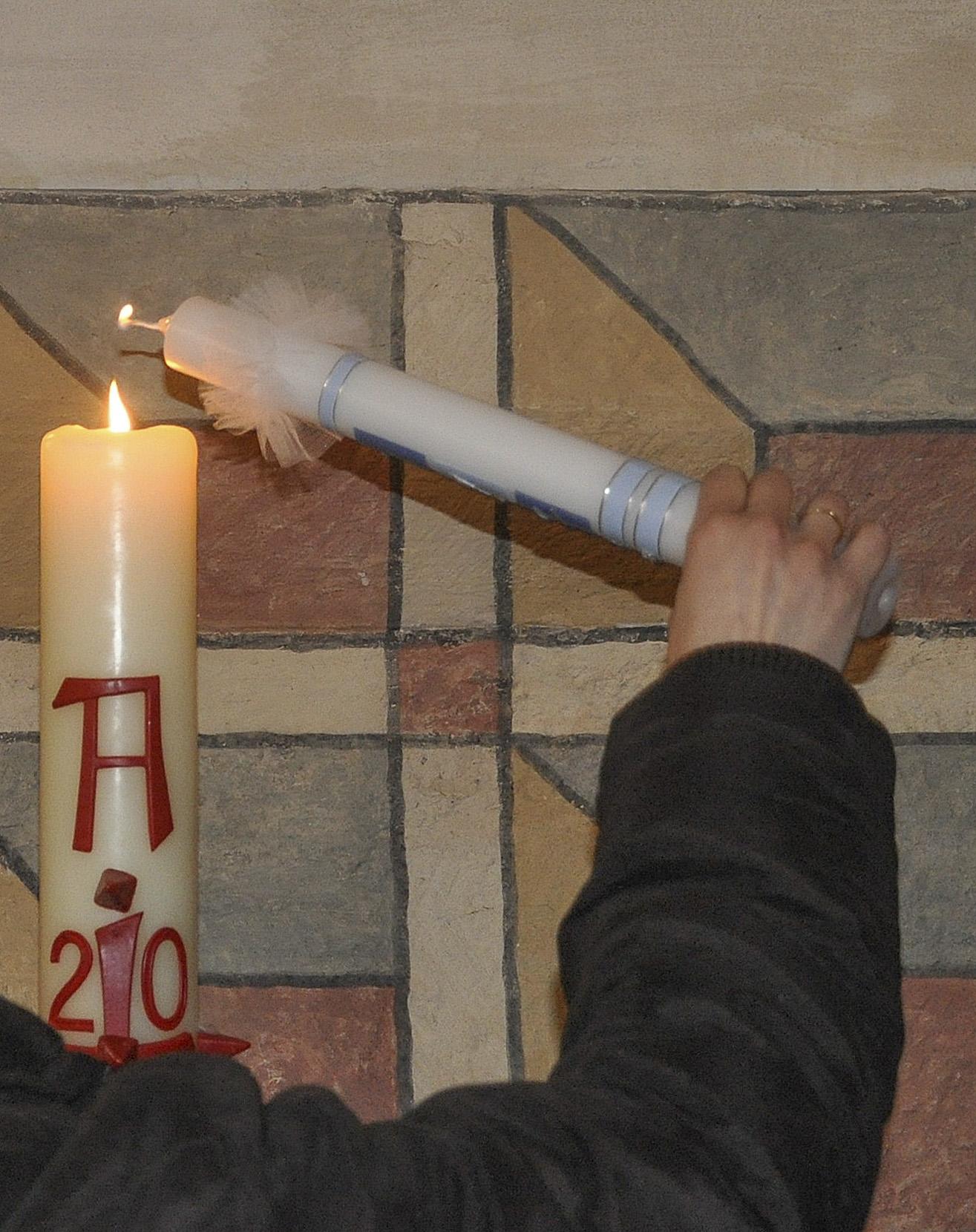 Eine Taufkerze wird an der Osterkerze angezündet