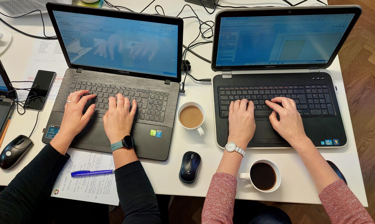Zwei Laptops auf dem zwei Händepaare tippen