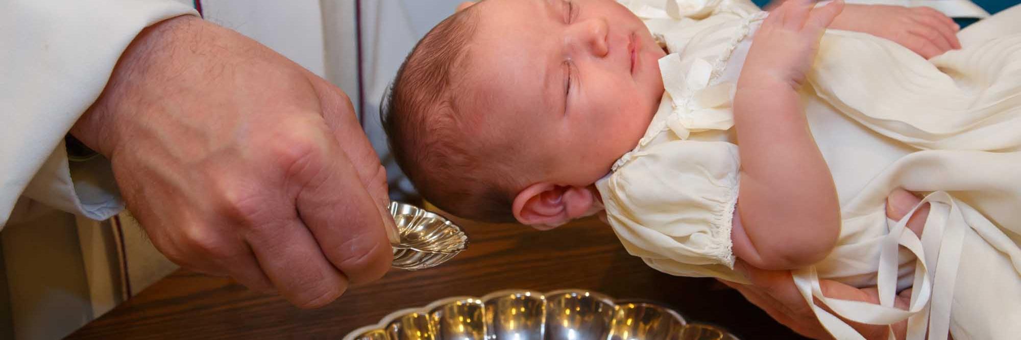 Einem über das Taufbecken gehaltenem Baby wird Wasser über den Kopf gegossen