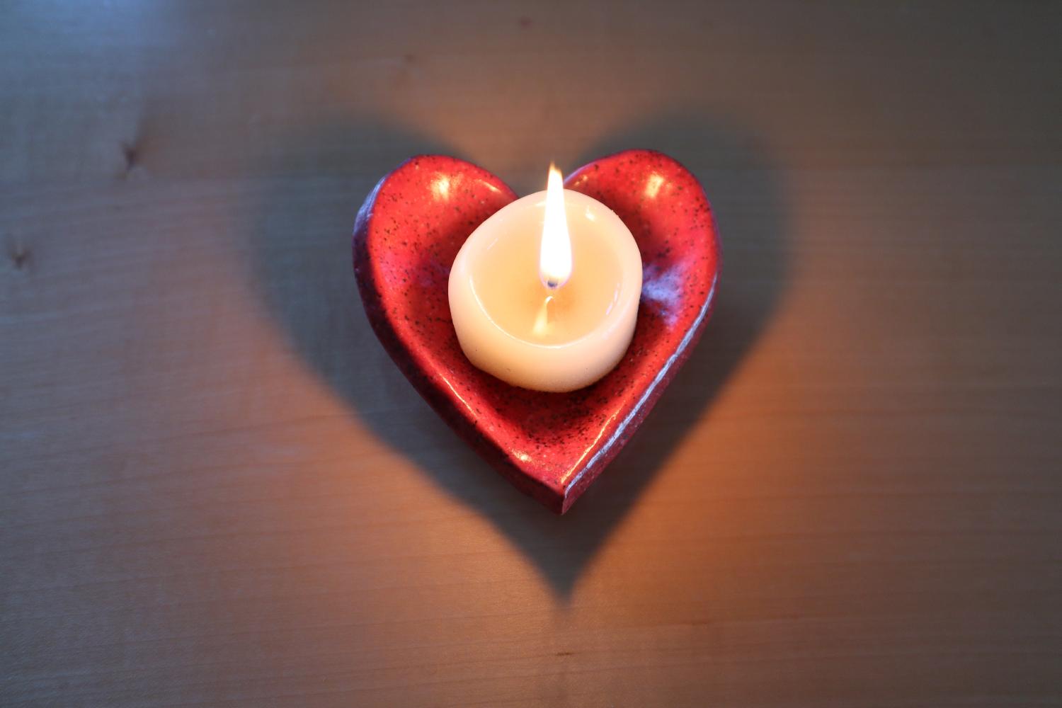 Brennende Kerze auf einer getöpferten Unterlage in Herzform