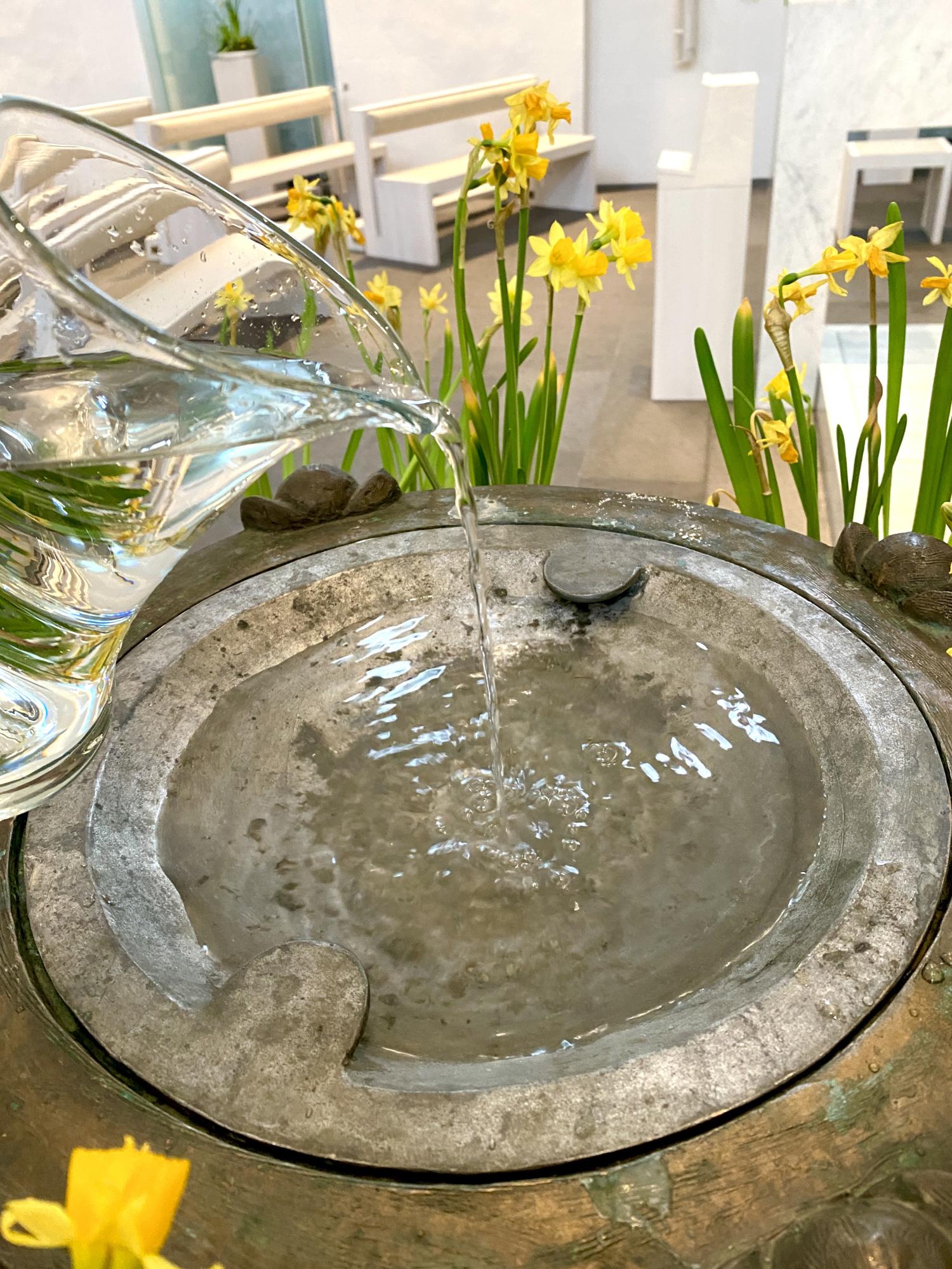 Eingießen von Weihwasser in ein Taufbecken