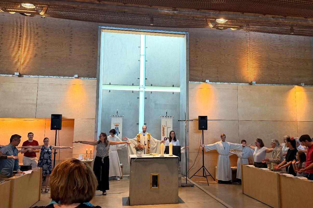 Pfarrer, Messdiener und Gläubige stehen um den Altar und reichen sich die Hände