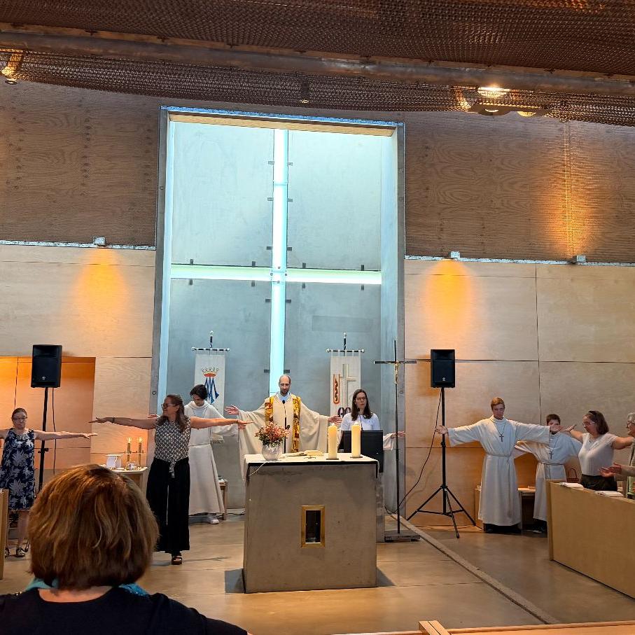 Pfarrer, Messdiener und Gläubige stehen um den Altar und reichen sich die Hände